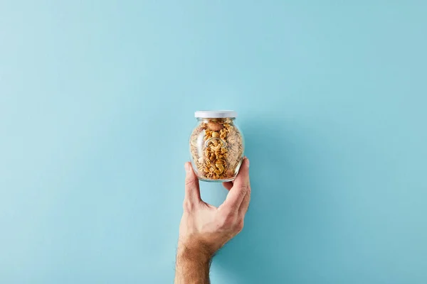 Vista cortada do homem segurando frasco de granola no fundo azul — Fotografia de Stock