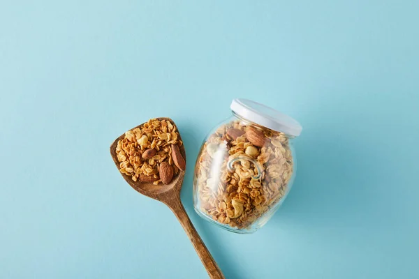 Top view of jar of granola with wooden spatula on blue background — Stock Photo