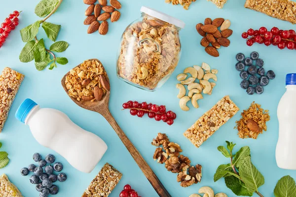 Draufsicht auf die Zusammensetzung von Nüssen, Flaschen Joghurt, Beeren, Müsliriegeln und Minze auf blauem Hintergrund — Stockfoto