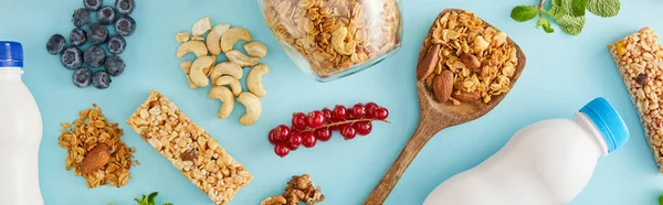 Top view of food composition of nuts, bottles of yogurt, berries, cereal bars and mint on blue background, panoramic shot — Stock Photo