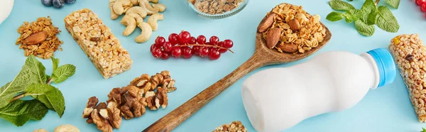 Nahrungsmittelzusammensetzung aus Nüssen, einer Flasche Joghurt, Beeren, Müsliriegeln und Minze auf blauem Hintergrund, Panoramaaufnahme — Stockfoto