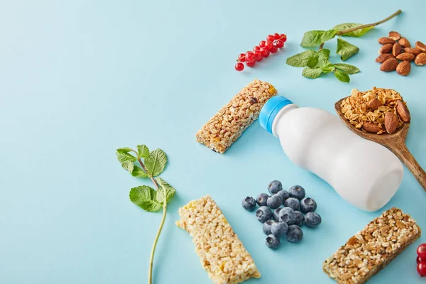 Botella de yogur, bayas, barritas de cereales, hojas de menta y almendras sobre fondo azul — Stock Photo