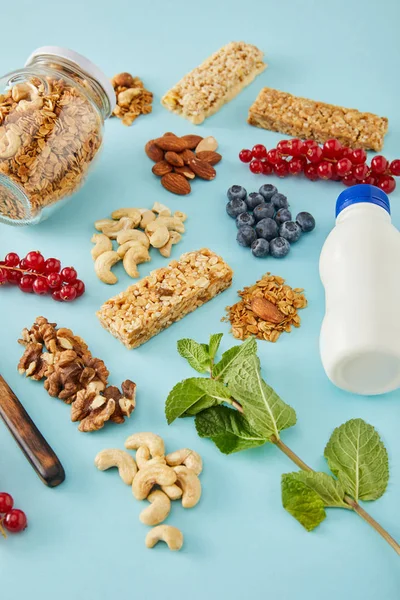 Бутылка йогурта, ягод, мяты, банки мюсли и орехов на голубом фоне — стоковое фото
