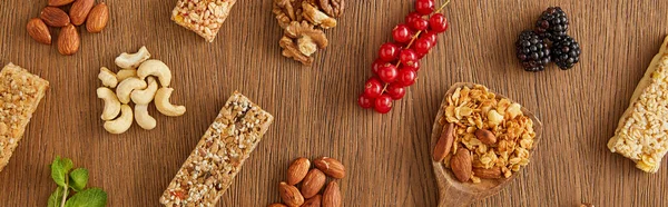 Vista superior de la composición de alimentos de bayas, nueces y barras de cereales sobre fondo de madera, plano panorámico - foto de stock