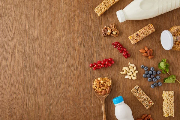 Vista superior de bayas, nueces, barras de cereales y botellas de yogur y leche sobre fondo de madera - foto de stock