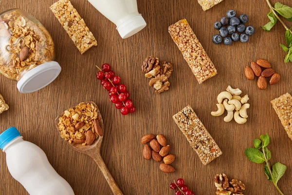 Vista superior de la composición de alimentos de bayas, frutos secos, barras de cereales y botellas de yogur y leche sobre fondo de madera — Stock Photo