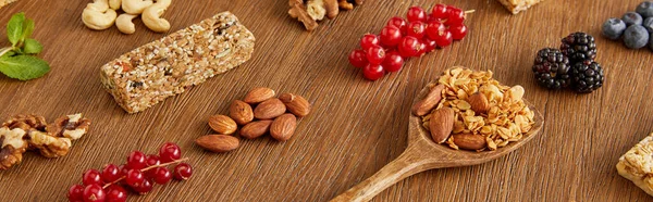 Berries, nuts, cereal bars and spatula with granola on wooden background, panoramic shot — Stock Photo
