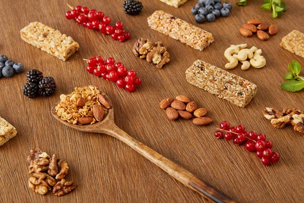 Bayas, nueces, barras de cereales y espátula con granola sobre fondo de madera - foto de stock