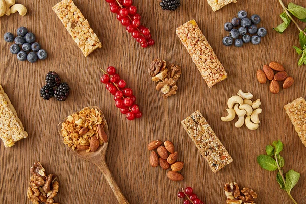 Vista superior da composição de alimentos de bagas, nozes, barras de cereais, hortelã e espátula com granola sobre fundo de madeira — Fotografia de Stock