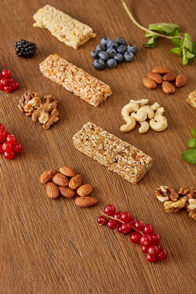 Selective focus of berries, nuts, cereal bars, mint on wooden background — Stock Photo
