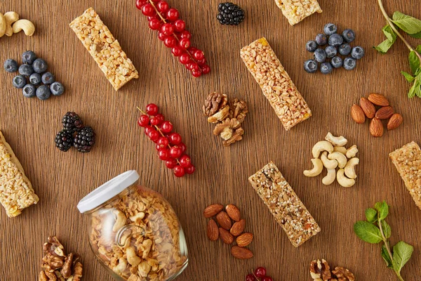 Vista dall'alto della composizione alimentare di bacche, noci, barrette di cereali, menta e barattolo di muesli su fondo di legno — Foto stock