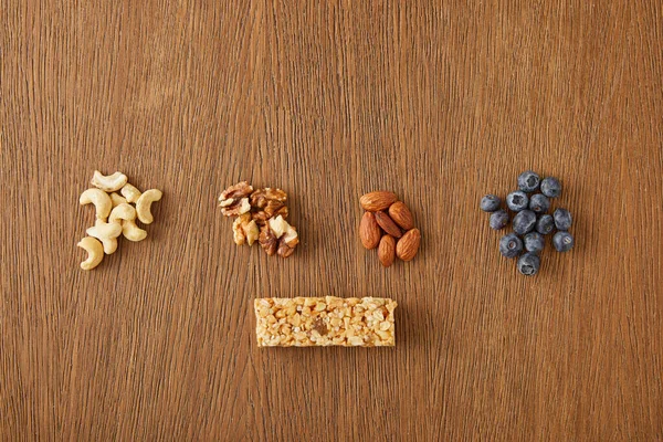 Vue de dessus des noix, amandes, noix de cajou, bleuets et barre de céréales sur fond en bois — Photo de stock