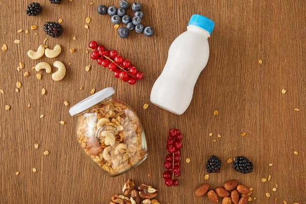 Draufsicht auf Beeren, Nüsse, Glas Müsli und eine Flasche Joghurt auf Holzgrund — Stockfoto