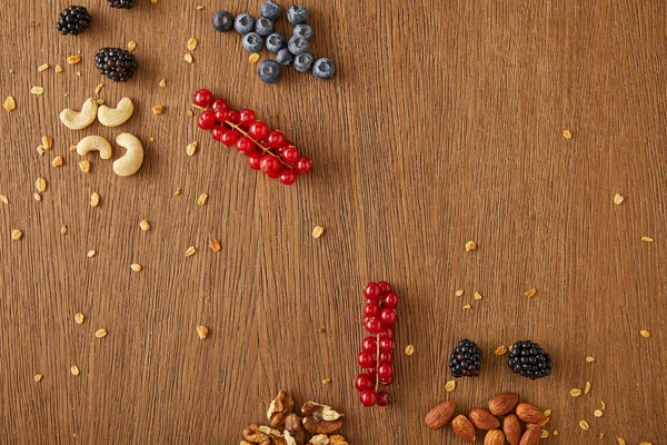 Draufsicht auf Blaubeeren, rote Johannisbeeren, Walnüsse, Mandeln, Cashewnüsse auf Holzgrund — Stockfoto