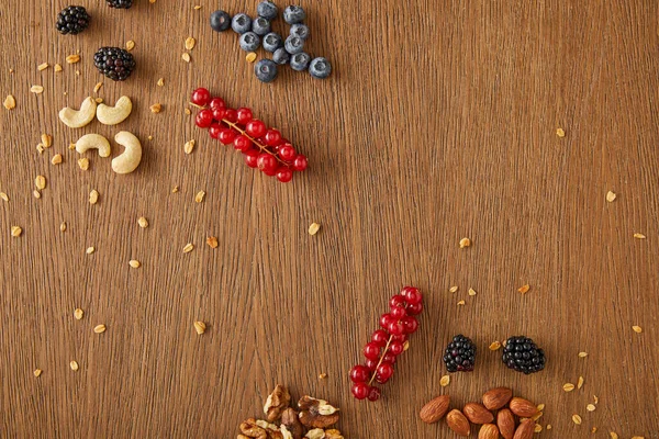 Vue de dessus des bleuets, groseilles rouges, noix, amandes, noix de cajou et flocons d'avoine sur fond en bois — Photo de stock