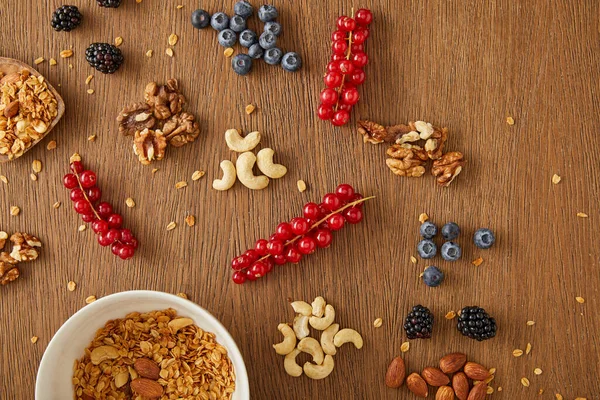Top view of bowl with granola next to berries, nuts and cereal bars on wooden background — Stock Photo