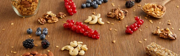 Arándanos, grosellas rojas, nueces, almendras, anacardos, barra de cereales sobre fondo de madera, plano panorámico - foto de stock