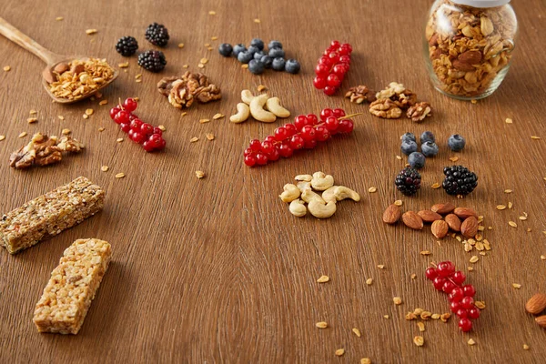 Vasetto di granola accanto a bacche, noci, barrette di cereali su fondo di legno — Foto stock