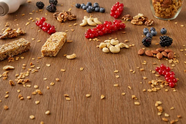 Grosellas rojas, arándanos, nueces, almendras, anacardos, copos de avena y barras de cereales sobre fondo de madera — Stock Photo