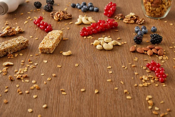 Rote Johannisbeeren, Blaubeeren, Walnüsse, Mandeln, Cashewkerne, Haferflocken und Müsliriegel auf Holzgrund — Stockfoto