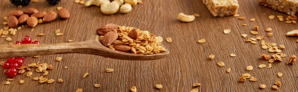 Wooden spatula with granola above table and nuts, oat flakes and berries on wooden background, panoramic shot — Stock Photo