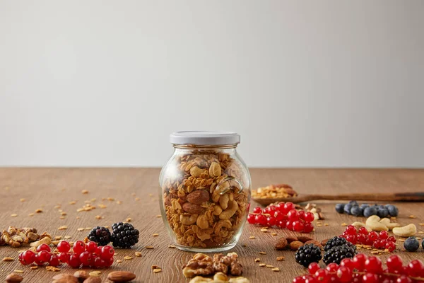 Foco seletivo de jarra de granola com nozes, flocos de aveia, bagas e barras de cereais em fundo de madeira isolado em cinza — Fotografia de Stock