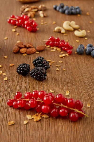 Selective focus of redcurrants, blueberries, oat flakes and nuts on wooden background — Stock Photo