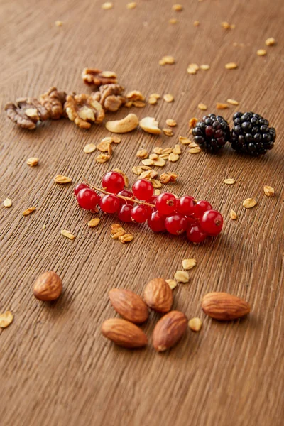 Amandes, noix de cajou, noix de Grenoble, groseilles rouges, mûres, flocons d'avoine sur fond bois — Photo de stock