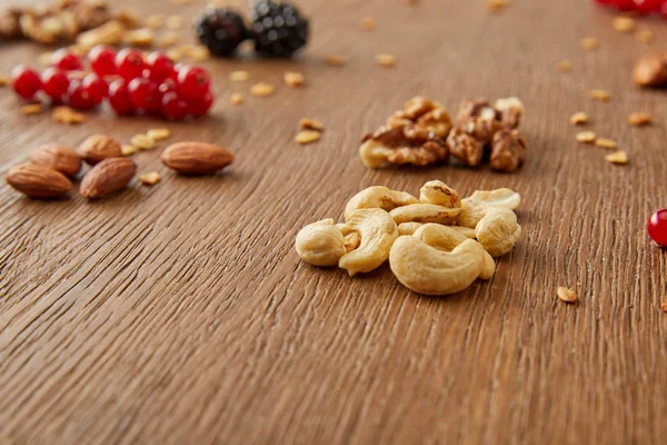 Selective focus of cashews with almonds, walnuts, redcurrants, blackberries on wooden background — Stock Photo