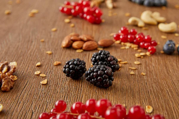 Selektiver Fokus von roten Johannisbeeren, Brombeeren, Cashewnüssen, Mandeln, Walnüssen auf Holzgrund — Stockfoto