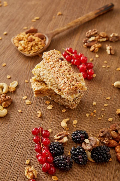 Enfoque selectivo de barras de cereales, espátula con granola, grosellas rojas, moras y nueces sobre fondo de madera - foto de stock