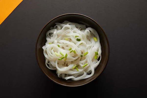 Top view of rice noodles in bowl on yellow and black surface — Stock Photo