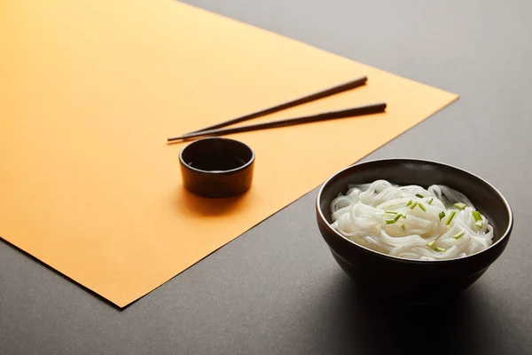 Selective focus of rice noodles in bowl near chopsticks and soy sauce on yellow and black surface — Stock Photo