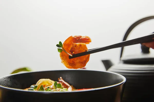 Обрезанный вид женщины, держащей креветки с палочками для еды рядом с лапшой в миске изолированы на сером — стоковое фото