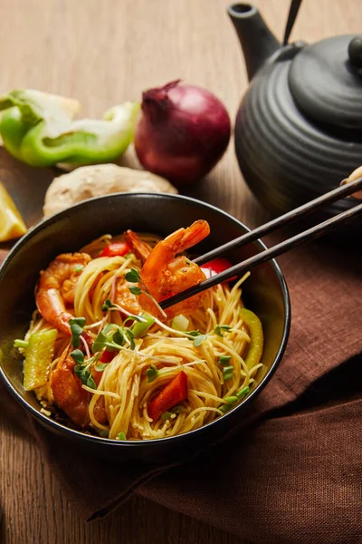 Cropped view of woman eating noodles with shrimps and vegetables with chopsticks — Stock Photo