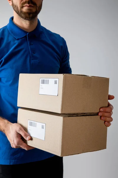 Vista recortada de mensajería con cajas de cartón con códigos qr y códigos de barras aislados en gris - foto de stock