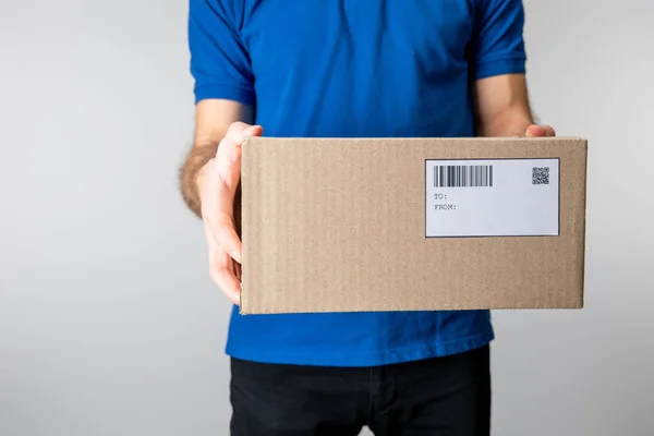 Cropped view of courier holding cardboard box with barcode and qr code isolated on grey — Stock Photo