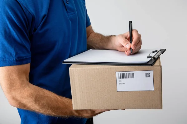 Cropped view of courier writing on clipboard and holding cardboard box isolated on grey — Stock Photo