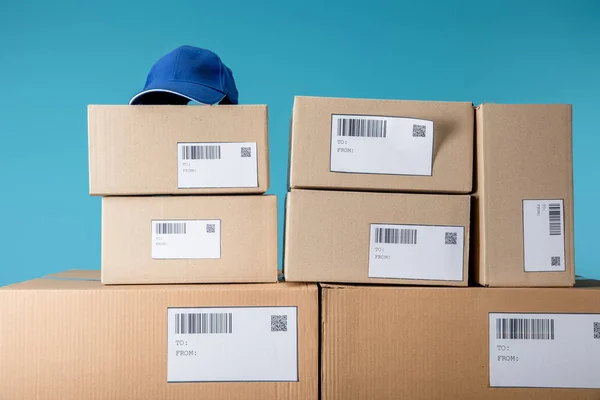 Cap on stacked cardboard packages with qr and barecodes isolated on blue — Stock Photo