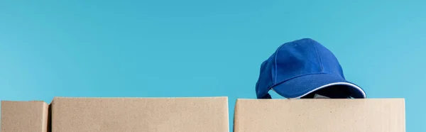 Casquette sur carton isolé sur plan bleu, panoramique — Photo de stock