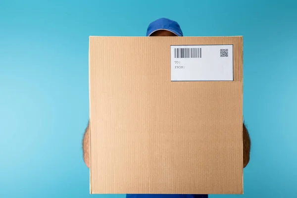 Courier holding cardboard box with qr and barcode isolated on blue — Stock Photo