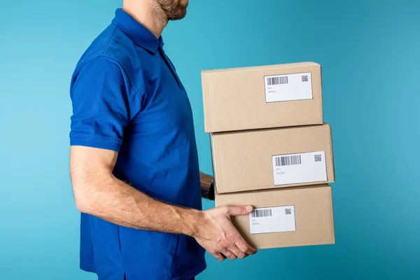 Vista lateral del repartidor que sostiene paquetes de cartón aislados en azul - foto de stock