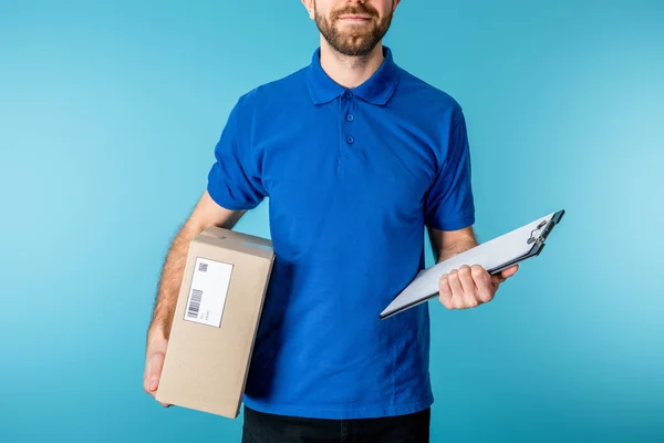 Coupé vue de courrier barbu tenant le presse-papiers et le paquet de carton isolé sur bleu — Photo de stock