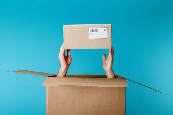 Vista recortada del mensajero que sostiene la caja de cartón del paquete aislado en azul - foto de stock