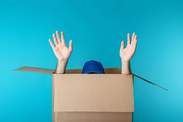 Hands and cap of delivery man in cardboard box isolated on blue — Stock Photo