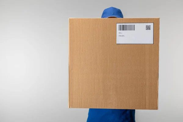 Delivery man in uniform holding cardboard box with qr code and barcode isolated on grey — Stock Photo