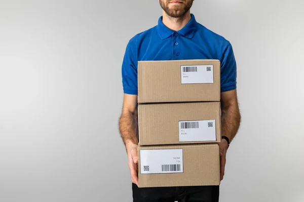 Cropped view of delivery man holding cardboard packages with qr codes and barcodes on cards isolated on grey — Stock Photo