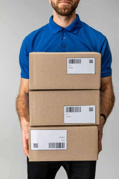 Cropped view of courier holding boxes with barcodes and qr codes isolated on grey — Stock Photo