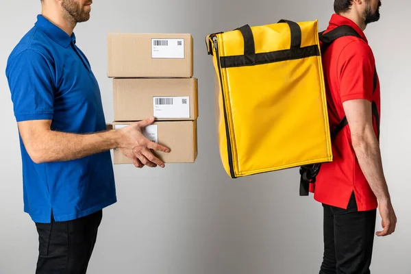 Vista lateral de correios com caixas de papelão e mochila térmica isolada em cinza — Fotografia de Stock