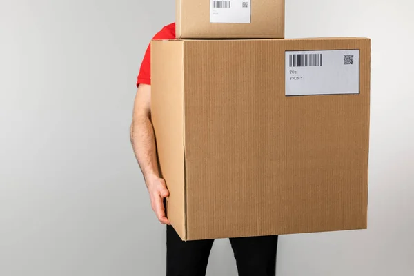 Entrega hombre celebración de cajas con códigos de barras y códigos qr en tarjetas aisladas en gris - foto de stock